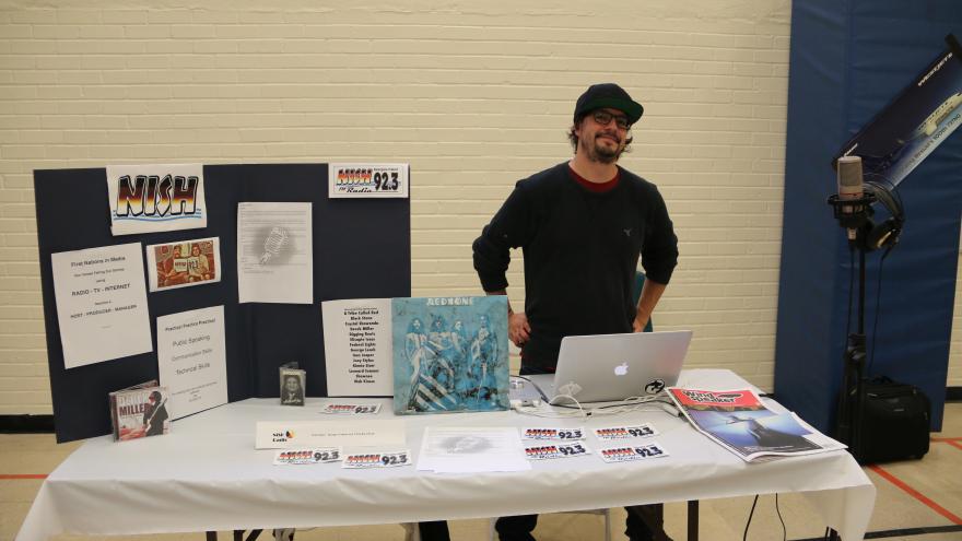 A man stands at a booth with materials about First Nations representation in media.