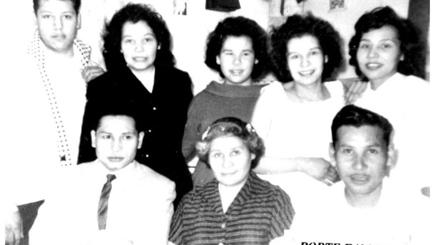 A vintage family photo with seven people, four women and three men, smiling indoors.