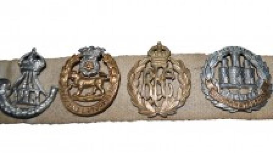Four military badges on a tan fabric strip, varying designs and colors.