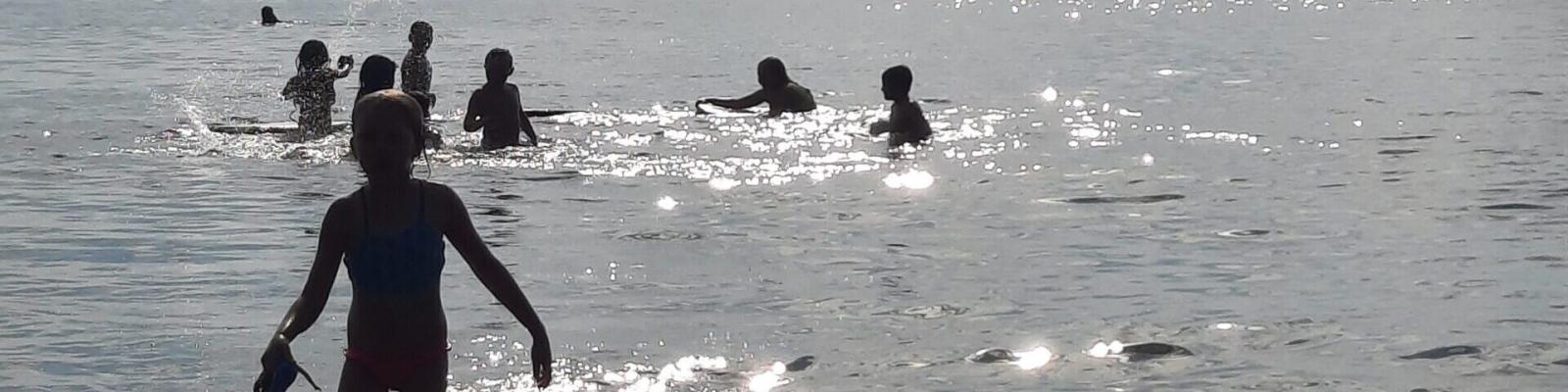 Silhouetted children swimming in a sunlit sea.