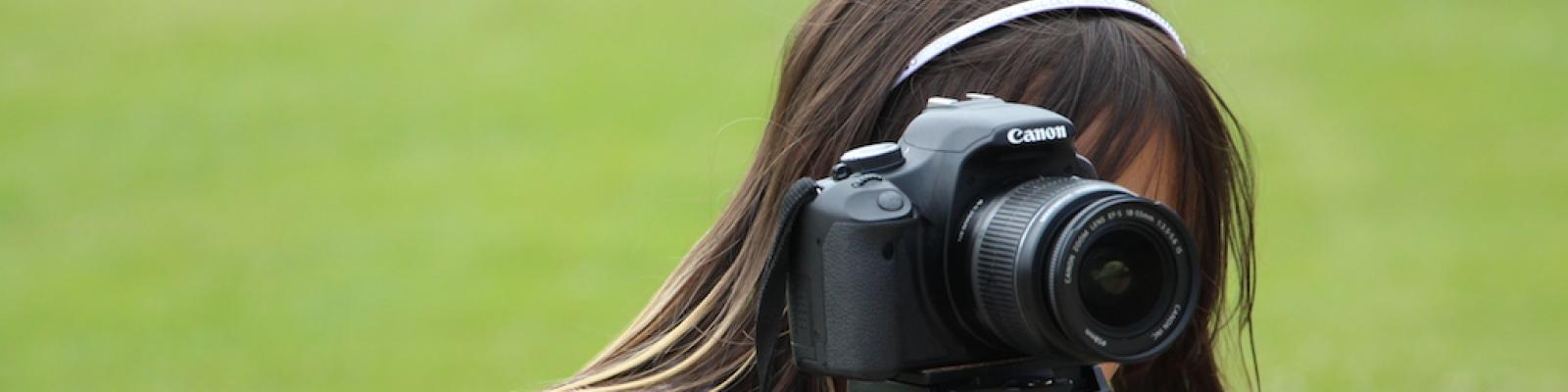 Young girl behind the viewfinder of a DSLR camera on a tripod.