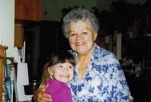 Grandmother and young girl smiling and hugging in a dimly lit room.