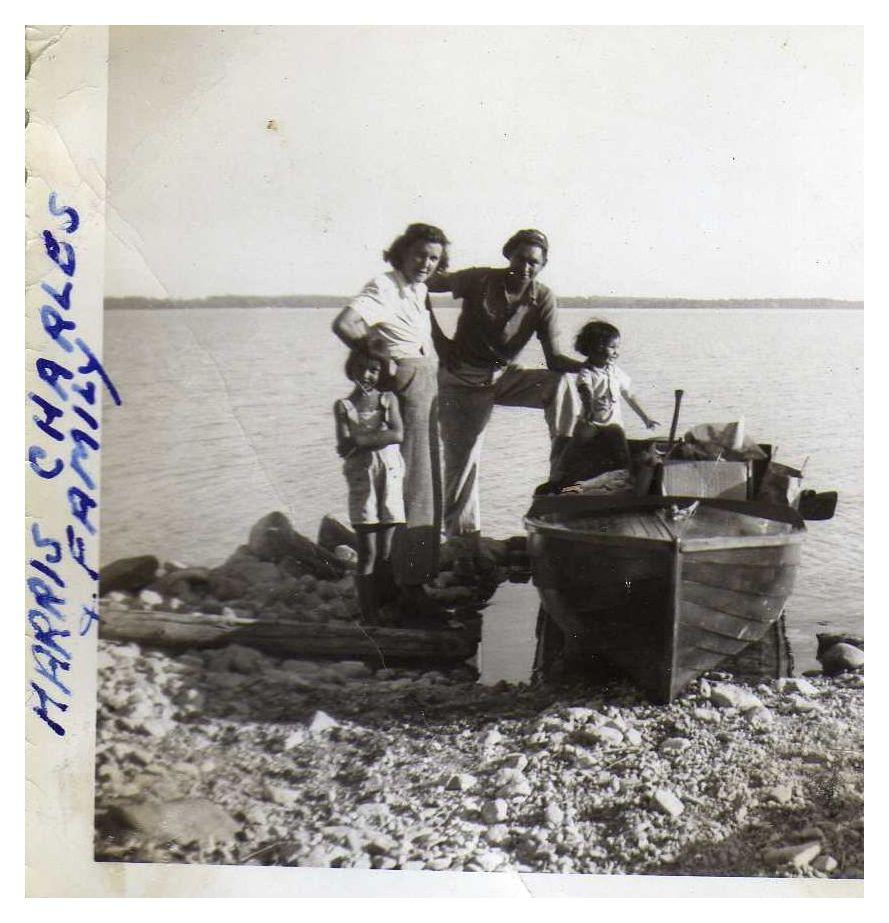 A family standing by a boat on a rocky lakeshore.