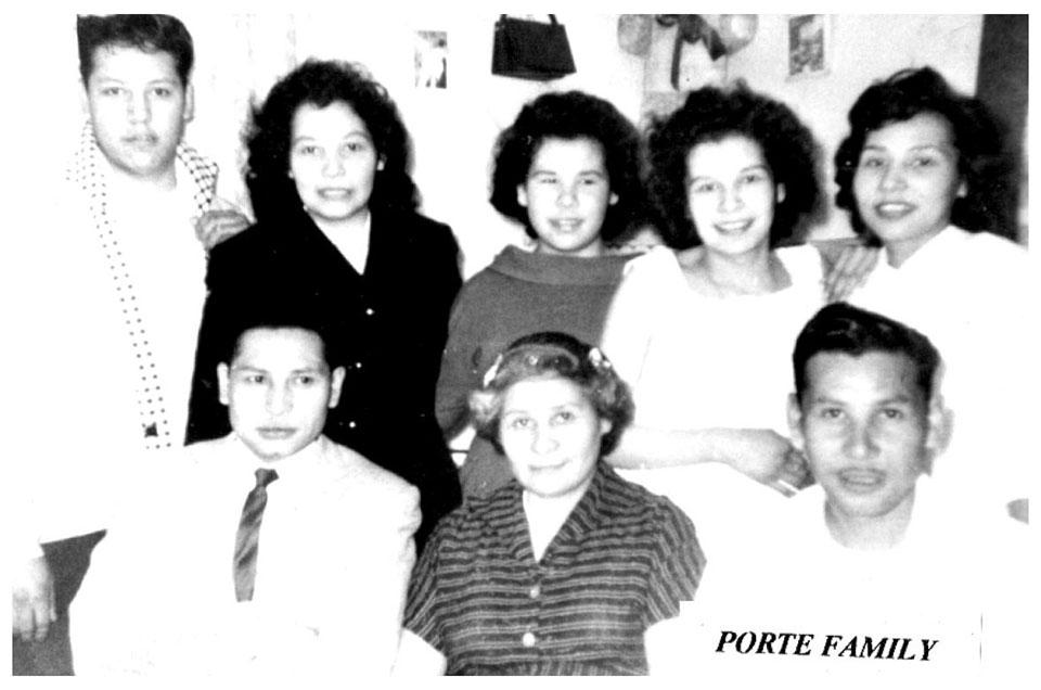A vintage family photo with seven people, four women and three men, smiling indoors.