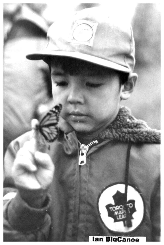 Child in cap observing butterfly on finger. Black-and-white photo.
