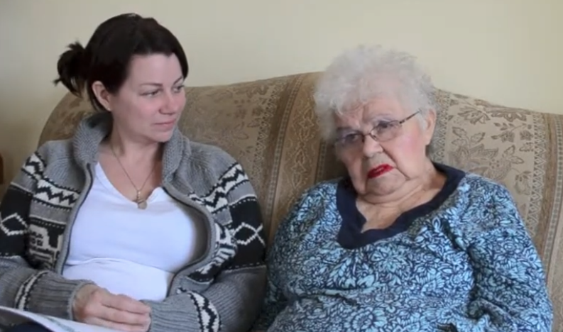 Two women sitting on a couch, one elderly, both with calm expressions.