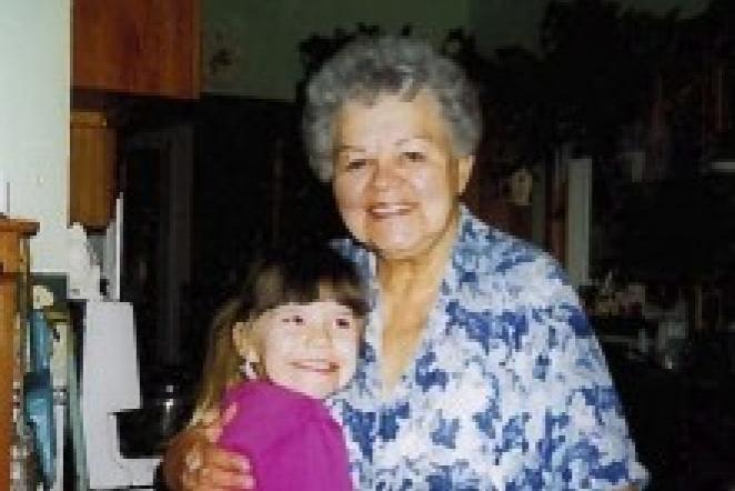 Grandmother and young girl smiling and hugging in a dimly lit room.