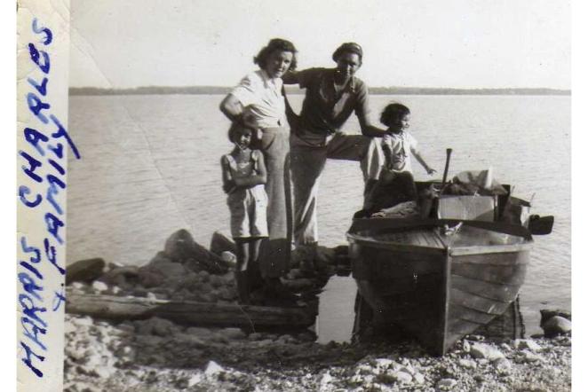 A family standing by a boat on a rocky lakeshore.