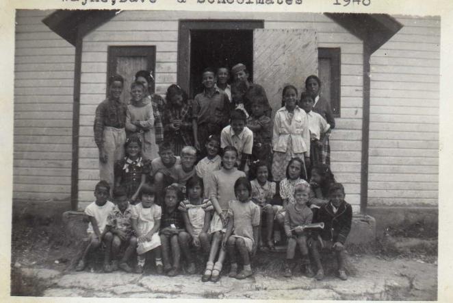 Group of children and adults posing in front of a wooden building, 1948.