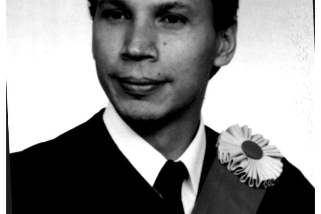 Black and white portrait of a man in a suit with a floral sash.