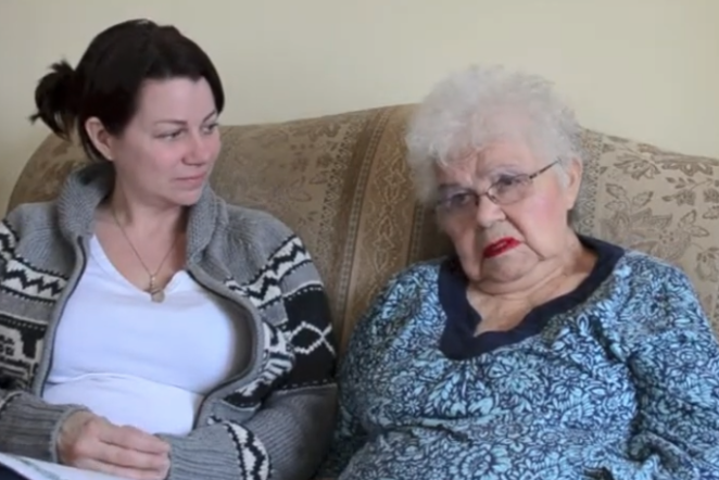 Two women sitting on a couch, one elderly, both with calm expressions.