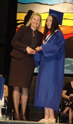 Graduation ceremony with a student in a blue cap and gown shaking hands with a woman.