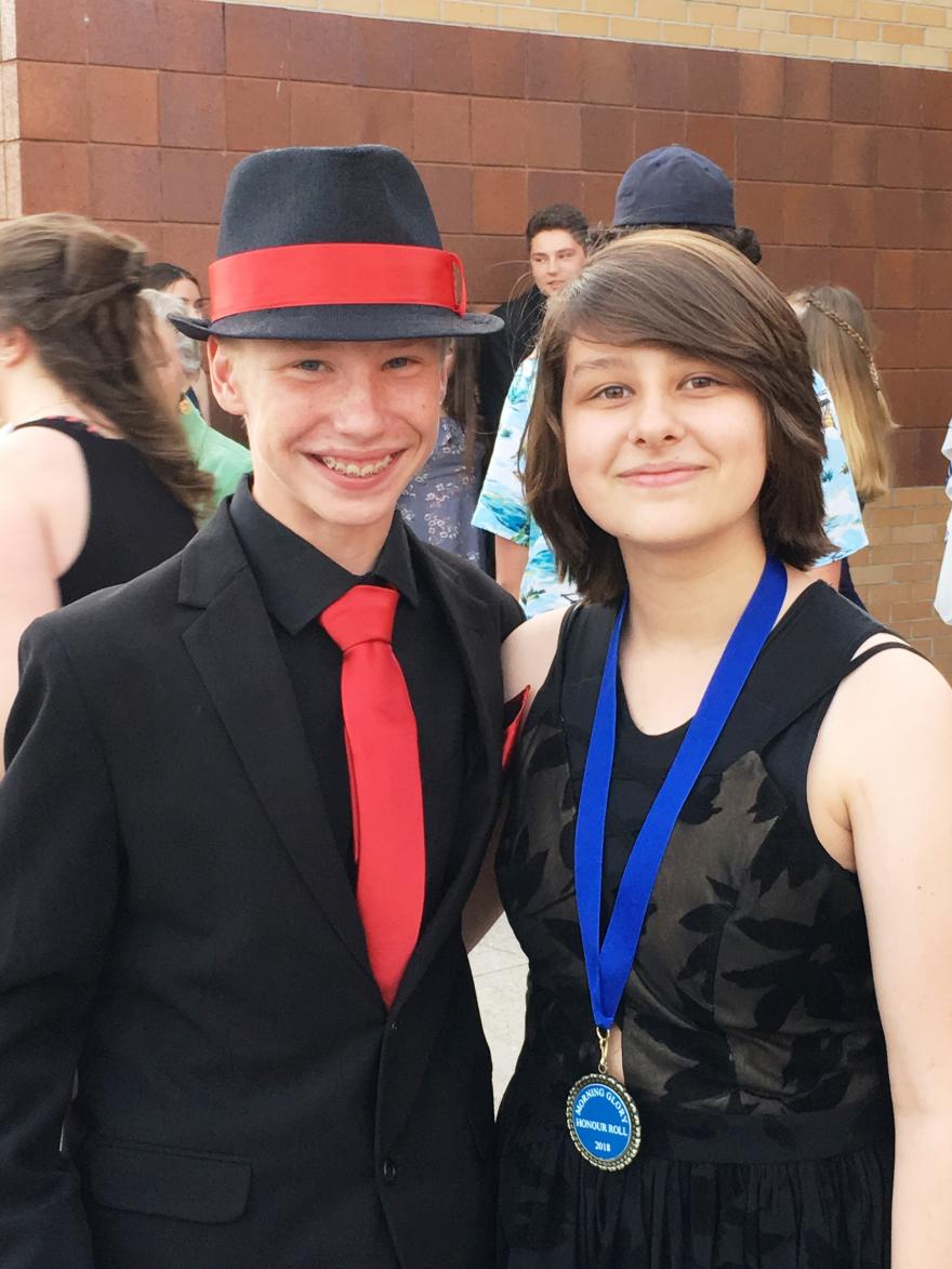 Two people smiling, wearing formal attire; one with a hat and red tie, the other with a medal.