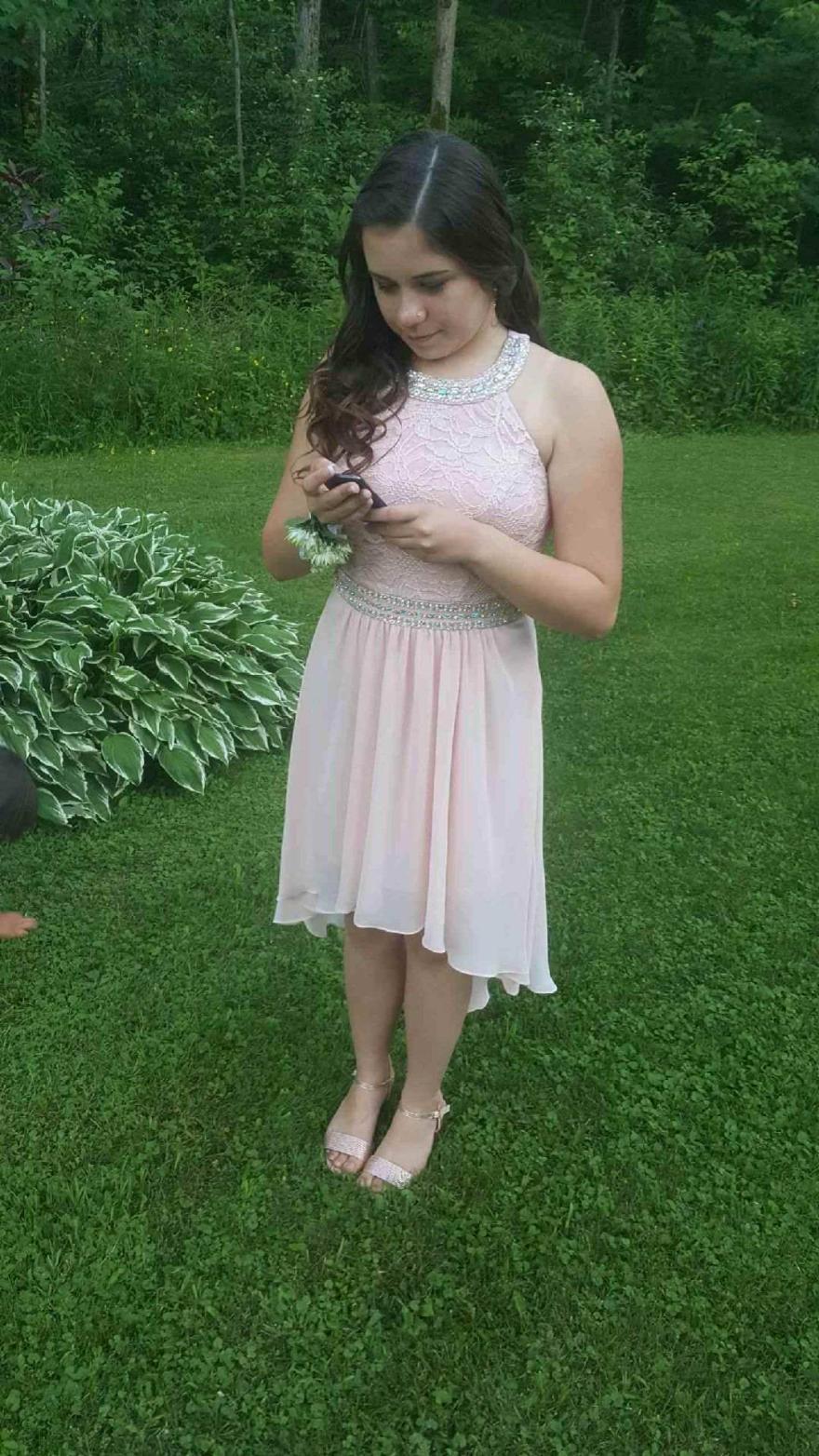 Young woman in a light pink dress stands on grass, looking at her phone.