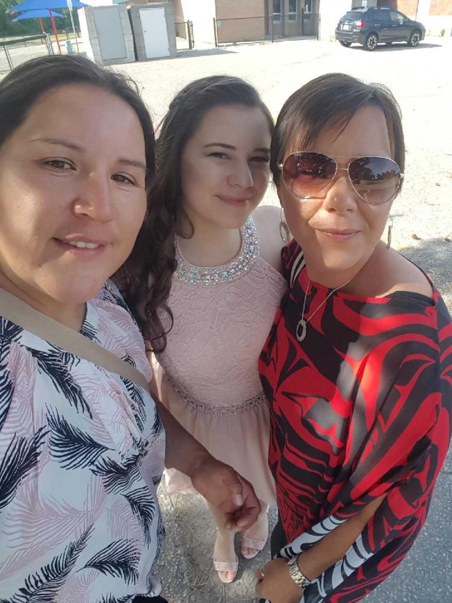 Three women smiling outdoors, one wears sunglasses, another a pink dress.