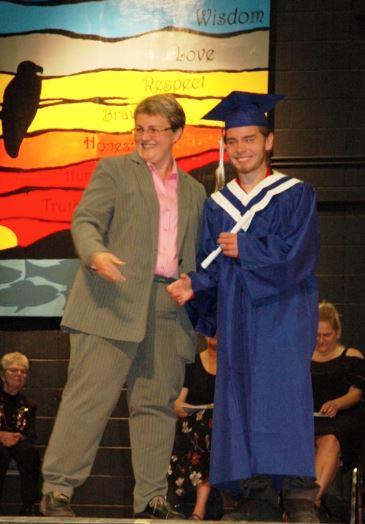 Graduation photo with a smiling student in blue robes shaking hands on stage.