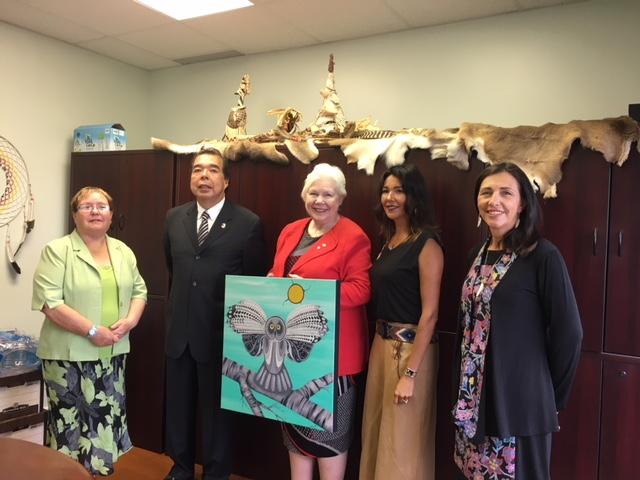 A group of five people in an office holding a colorful painting.