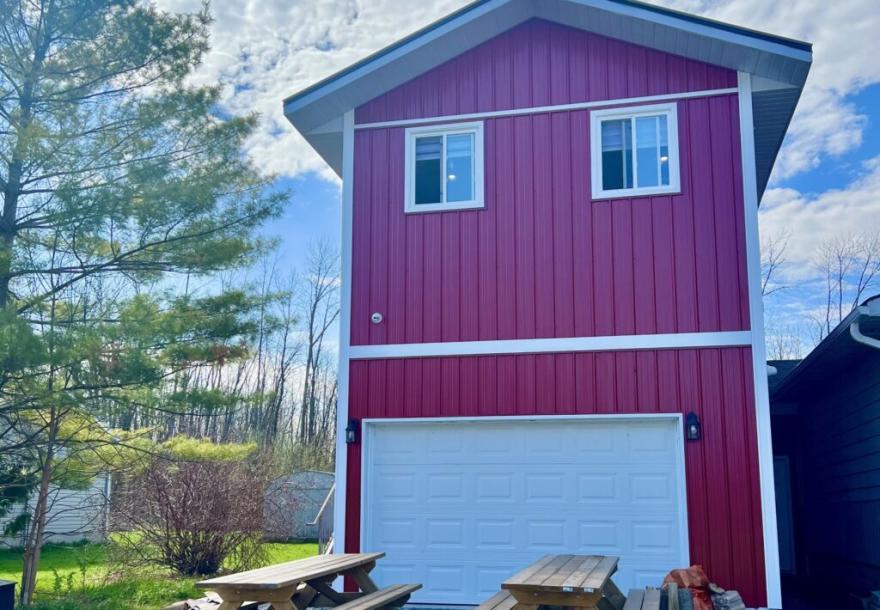 Red barn-style building with white trim, two windows, blue sky, and trees in the background.